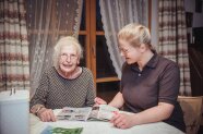 Seniorin und junge Frau sitzen am Tisch vor einer Zeitschrift
