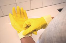 Person zieht sich Reinigungshandschuh über die Hand.