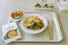 Tablett mit Nudelgericht und Beilagensalat, daneben Werbematerial zur Aktion Heimatteller 