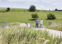 Bild zwei Menschen in einer grünen Landschaft, einer deutet auf etwas in der Ferne..