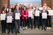 Eine Gruppe von Menschen steht auf der Treppe mit Landwirtschaftsministerin Michaela Kaniber und halten eine Urkunde