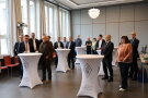 Menschen stehen in einem Sitzungssaal an Stehtischen
