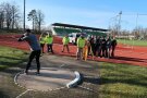 Ein Kugelstoßer, Schülerinnen und Schüler mit Messgeräten im Hintergrund