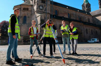 Schülerinnen und Schüler in Warnwesten arbeiten an einem Tachymeter. 