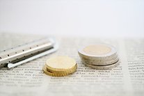 Gestapelte Münzen auf einem Zeitungsausschnitt und ein Kugelschreiber.
