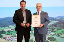 Ein Mann hält eine Medaille, ein weiterer eine Urkunde.