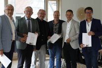 Sechs Männer nebeneinander mit Broschüren in der Hand 