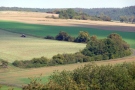 Leicht hängige Lage mit Feldern und zahlreichen Heckenstrukturen. Ein Schlepper mit einem Anbaugerät bei der Feldbestellung.