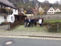 Die ILE-Managerinnen und –Manager stehen zusammen mit dem Bürgermeister vor der Stadtmauer und Häusersilhouetten in Pottenstein. Im Hintergrund Felsformationen an einem steilen Hang. 