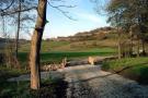 Im Vordergrund ein neu geschotterter Feldweg, der von Einzelbäumen gesäumt wird und über eine kleine Brücke führt, im Hintergrund reich gegliederte Kulturlandschaft.