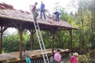 Auf einen neu gedeckten Dach stehen drei Männer. Eine Leiter lehnt an der Dachreling. 