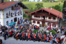 Fest auf dem neuen Dorfplatz. Viele Menschen sitzen an Biertischen vor einem Gasthaus und einem Wohnhaus