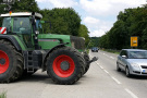 Traktor steht an der Einmündung vom landwirtschaftlichen Weg zur Staatsstraße. Der vorbeifahrende Kleinwagen ist nicht höher als das Vorderrad des Traktors.