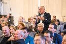Mann steht im Publikum mit Mikrofon in der Hand und stellt eine Frage.